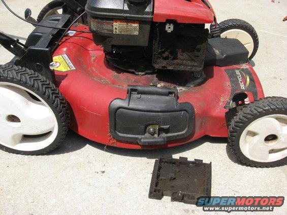Red lawn mower with a black engine and four wheels. A small black cover is detached and lying on the ground