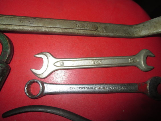 Three metal wrenches on a red surface. One has "BMW" and "13" stamped on it