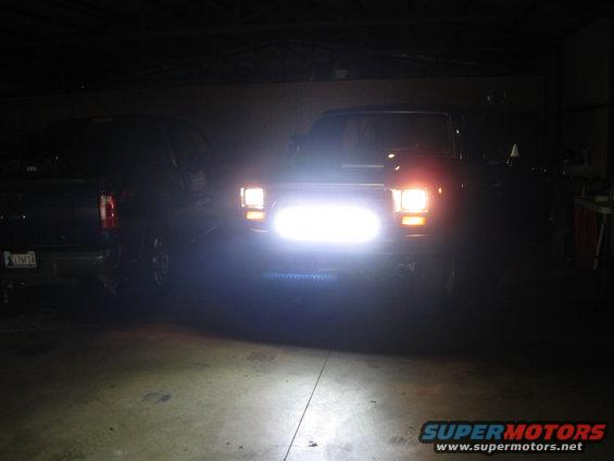 Two trucks in a garage, one with bright headlights on
