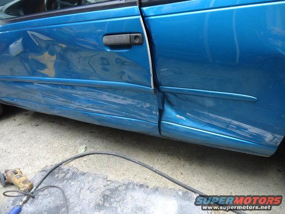 Blue 1994 Ford Thunderbird side door and fender with significant damage, showing a grinding tool on the ground
