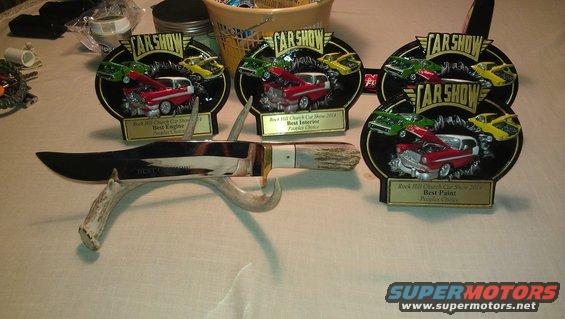 Car show trophies for Best Engine, Best Interior, and Best Paint next to a large knife