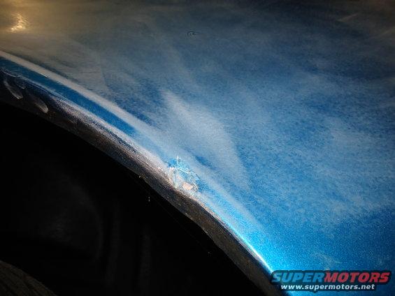 Close-up of a damaged blue car fender with chipped paint near the wheel well