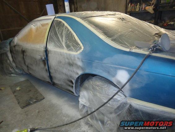 Blue 1994 Ford Thunderbird coupe covered in plastic and tape, with a spray gun attached to the side