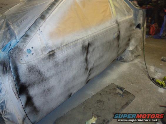 Side view of a car door covered in primer and masking tape, undergoing bodywork