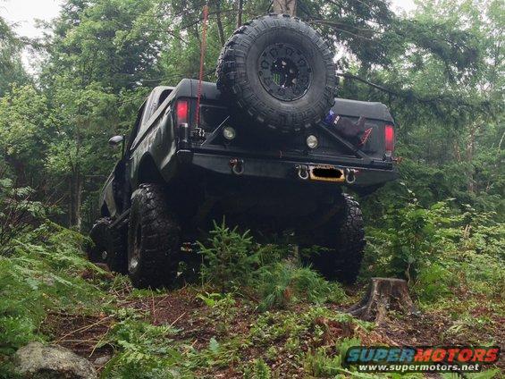 Black off-road SUV with large tires and a spare tire mounted on the back, driving on a wooded trail