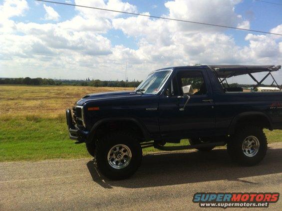 Dark blue Ford Bronco with a soft top, lifted suspension, and aftermarket wheels parked on a roadside