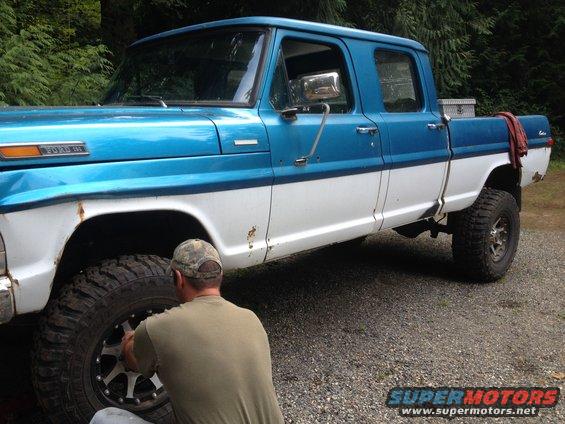Blue and white Ford F-Series truck with a man working on the front tire