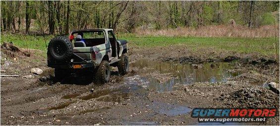 1978 Ford Bronco with spare tire on rear bumper driving through mud puddle