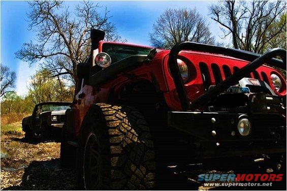 Red Jeep Wrangler with snorkel and winch parked on a dirt road, another dark vehicle in background