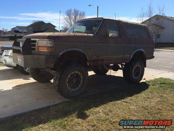 1993 Ford Bronco with aftermarket bull bar bumper, lifted suspension, and large tires parked next to a silver SUV