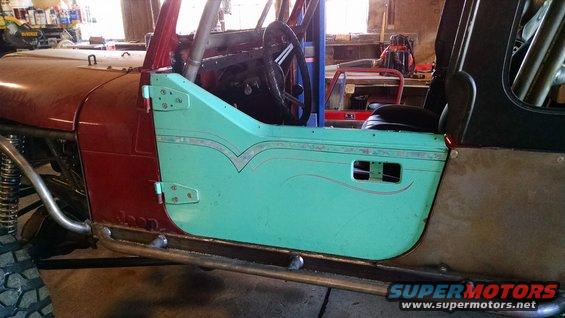 1985 Jeep CJ7 interior showing dashboard, steering wheel, and teal door with pinstriping. Roll cage visible