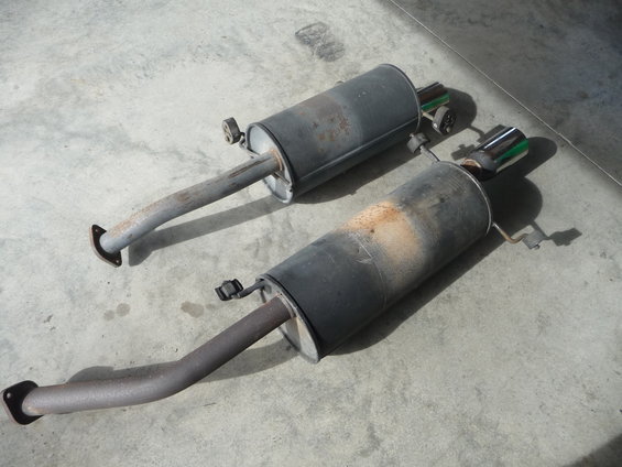 Two used exhaust mufflers with chrome tips, resting on a concrete surface