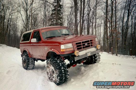 1995 Ford Bronco with oversized tires driving in a snowy forest
