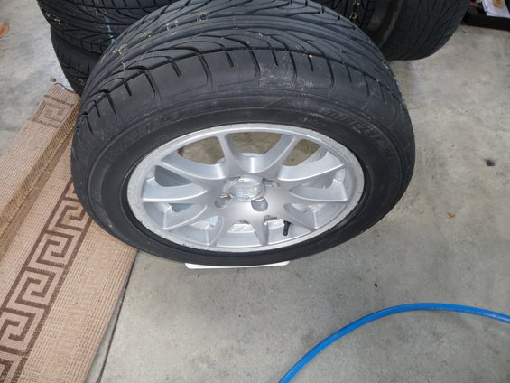 Stack of tires with a silver 5-spoke alloy wheel in the foreground