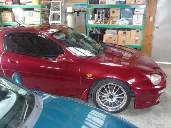 1993 Mazda MX-3, 2.5-V6 badge visible, parked next to a teal car in a garage