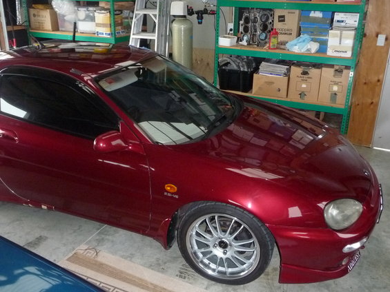 Red 1993 Mazda MX-3 coupe, 3/4 front view, parked indoors