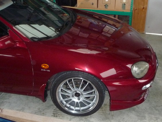 Red sports coupe, front fender has a 2.5i-V6 badge. Aftermarket wheels and body kit