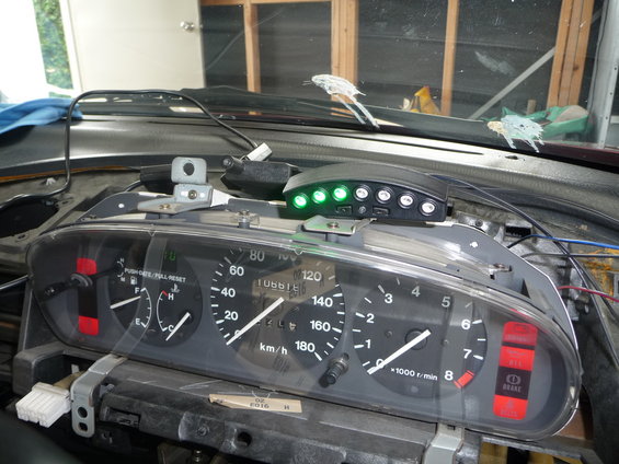 Interior view of car dashboard with speedometer, tachometer, and aftermarket device with green lights
