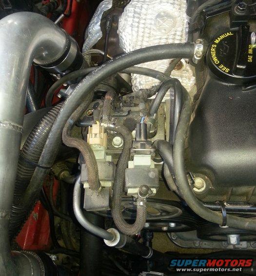 Close-up of engine bay showing turbo piping, hoses, and engine components. Text on oil cap reads 'SEE OWNER'S MANUAL'