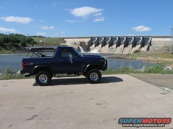 1982 Ford Bronco parked on concrete ramp with dam and water in background