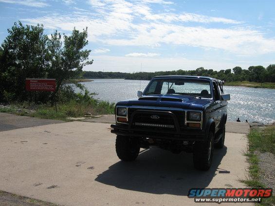 Blue SUV parked on concrete ramp near water, with a red sign to the left