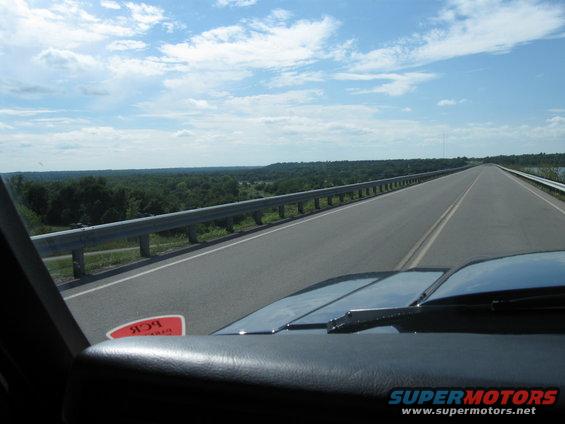 Dashboard and hood of a vehicle on a highway, with a red sticker on the windshield