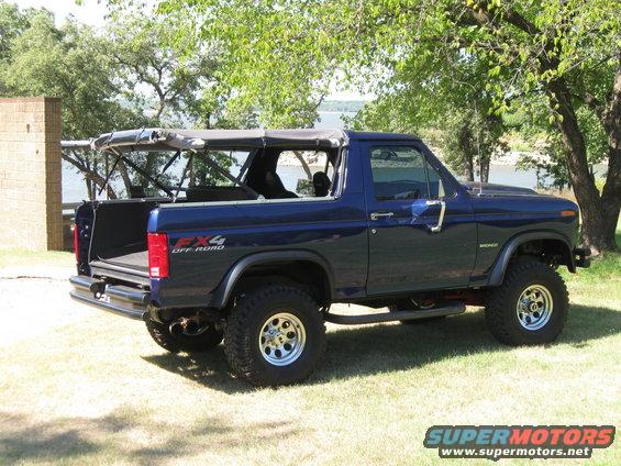 Blue Ford Bronco with soft top removed, parked on grass near water