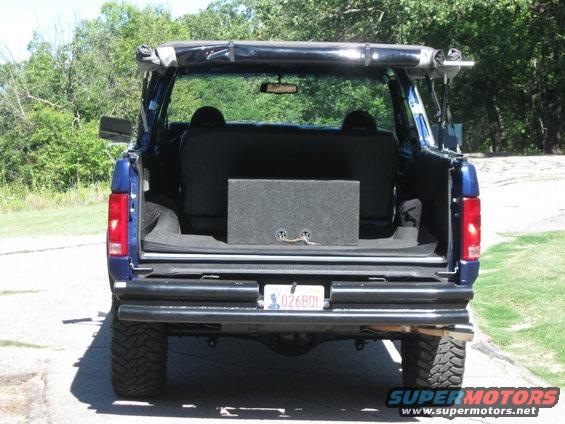 Blue Ford Bronco rear view with aftermarket bumper and spare tire carrier, aftermarket subwoofer box in cargo area