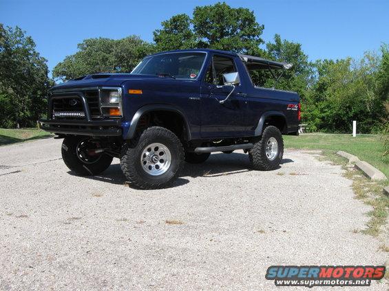 Dark blue Ford Bronco with aftermarket bumper and light bar, lifted suspension, and off-road tires