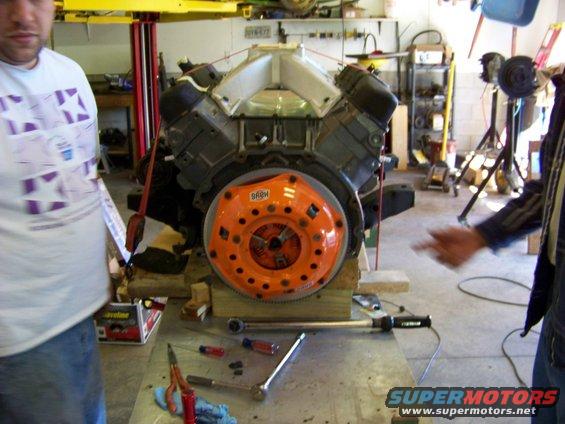 Engine with orange clutch assembly, tools on table, two people present