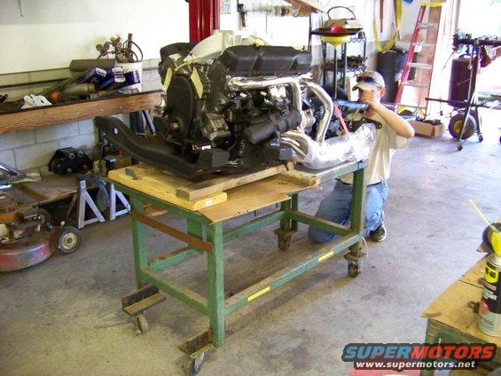 Engine on a green cart with a person working on it in a garage