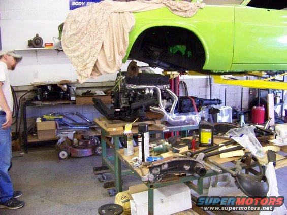 Lime green 1974 Dodge Challenger body on lift, engine on stand below, man looking