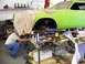 1974 Dodge Challenger - A mechanic works on the engine of a bright green 1974 Dodge Challenger, which is raised on a lift in a workshop.