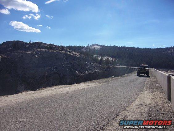 Black 1968 Ford Bronco driving on a road with a rocky hillside