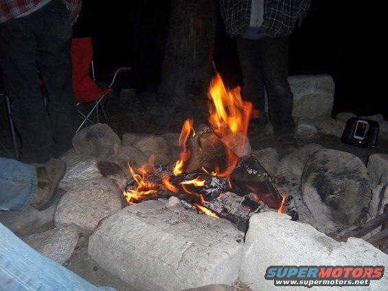 Campfire burning in a stone pit with people sitting around it at night