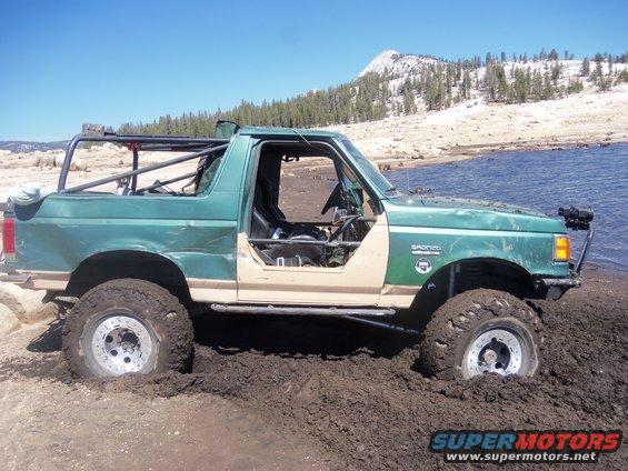 Green Bronco stuck in mud near water, roll cage installed, doors removed