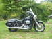 1998 Honda Shadow VT750C - A black cruiser motorcycle with saddlebags and a windshield is parked on a grassy lawn with trees in the background.