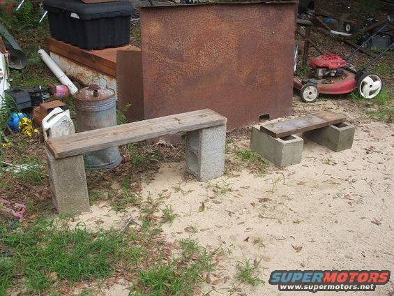 Red lawnmower with white wheels parked on sandy ground next to a rusty metal structure