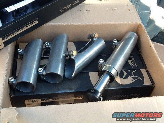 Four metal exhaust tips and Fox shock absorbers in a cardboard box
