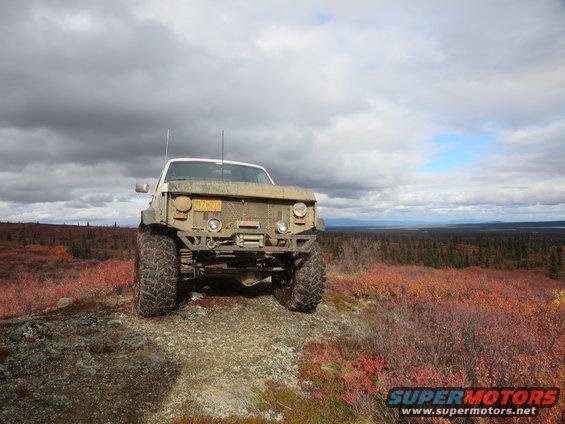 Modified pickup truck with large tires parked on a rocky, brush-covered hill