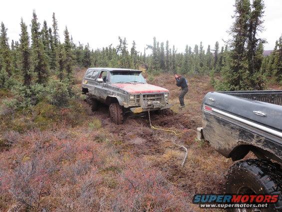 Two trucks stuck in mud, one is being pulled by the other