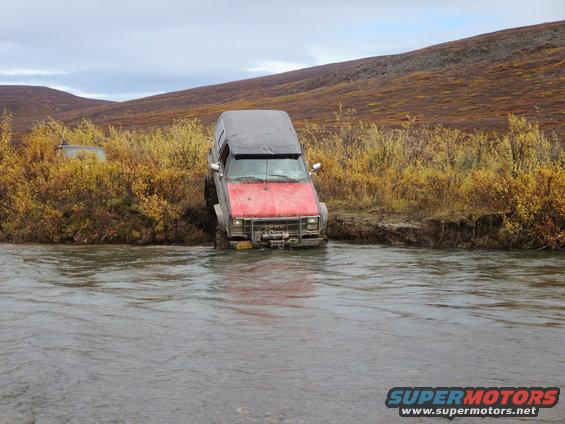 Off-road vehicle with red hood and gray body stuck in a river, front grille visible