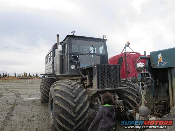 Tractor with large tires and a red trailer, viewed from the front