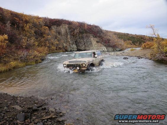 Ford Bronco driving through a river with fall foliage on the banks