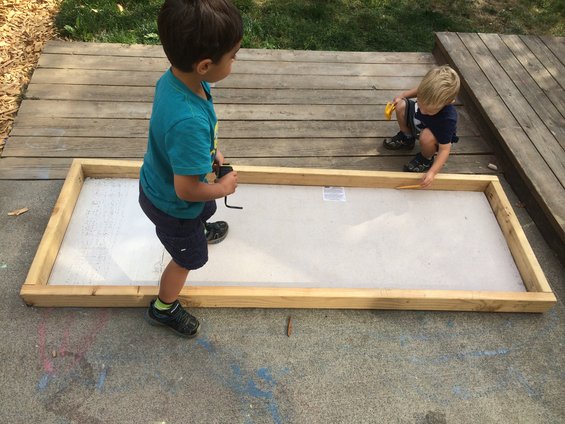 Two young boys are playing in a backyard area with a wooden frame on the ground