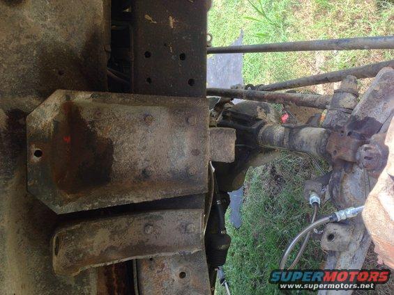 Close-up of rusty vehicle frame and front axle components, including steering linkage and brake lines
