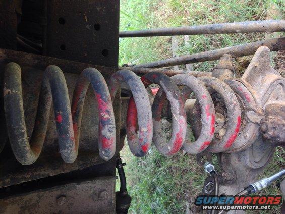 Suspension coil spring with red and blue paint marks, attached to a dirty axle