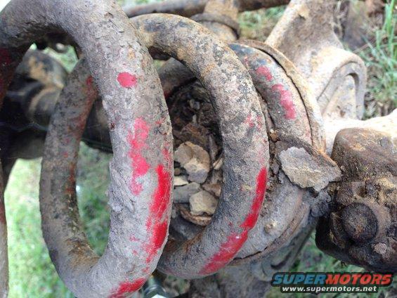 Close-up of a rusty coil spring with red paint marks, likely a vehicle suspension part