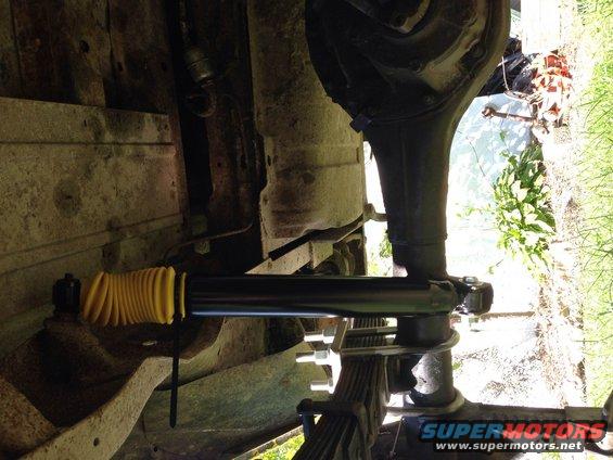 Undercarriage view of a yellow-bellowed shock absorber on a leaf spring suspension