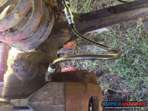 Close-up of a vehicle's brake caliper and flexible hose, with suspension components visible